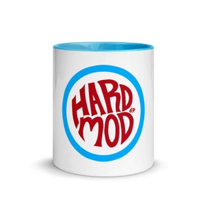 Puede incluir: Taza de cerámica blanca con interior azul y un círculo azul alrededor del texto rojo "HARD MOD 69". La taza es de tamaño estándar para café o té.