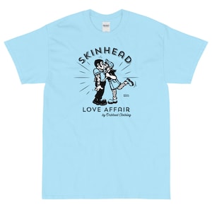 May include: A light blue t-shirt with a black and white illustration of a couple kissing. The illustration is surrounded by a circle with the text "SKINHEAD LOVE AFFAIR by Orblood Clothing".