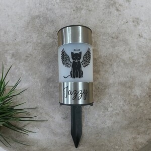 May include: A silver solar-powered memorial light with a black cat with wings and a halo. The light has the name "Jazzy" engraved on it.