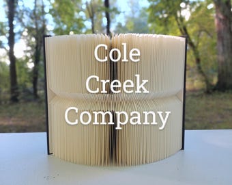 Może przedstawiać: Biała książka złożona w dekoracyjny kształt z nadrukowanym tekstem "Cole Creek Company" na okładce.