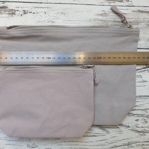 May include: Two zippered pouches made of a light gray canvas fabric. The pouches are nested inside each other, with the smaller pouch on top. A ruler is placed on top of the pouches, showing the larger pouch is approximately 30 inches wide.