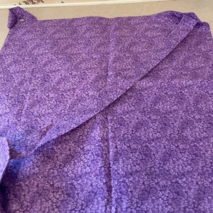 May include: A purple fabric with a small white floral pattern. The fabric is folded in half and has a seam along the edge.