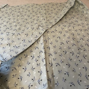 May include: A green fabric picnic blanket with a white and black swallow pattern. The blanket is folded in half and has a seam down the center.
