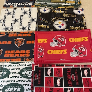 May include: Set of ten fabric coasters featuring various NFL team logos, including the Broncos, Cowboys, Steelers, Bears, Chiefs, Jets, and Razorbacks. The coasters are made of a soft, durable fabric and are perfect for protecting your furniture from spills and scratches.