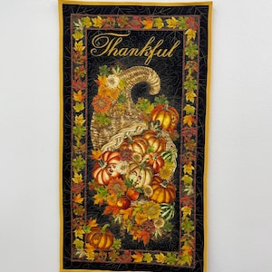 May include: A black and gold quilted wall hanging with a cornucopia overflowing with pumpkins, apples, and fall leaves. The word "Thankful" is written in a decorative script.