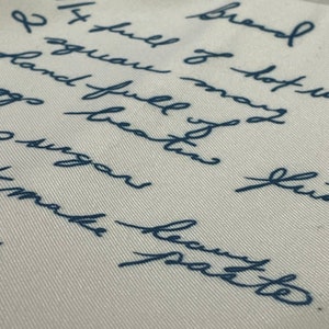 May include: A close-up of a white fabric surface with blue handwritten text that reads "Brand I squau may land full of hot gs beaten fus 14 full of hot make batte".