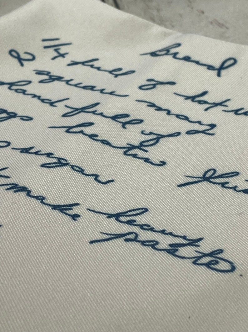May include: A close-up of a white fabric surface with blue handwritten text that reads "Brand I squau may land full of hot gs beaten fus 14 full of hot make batte".