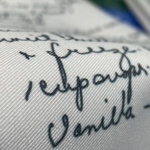 May include: White fabric with black handwritten text that reads "I'm free, I'm happy, I'm vanilla!"