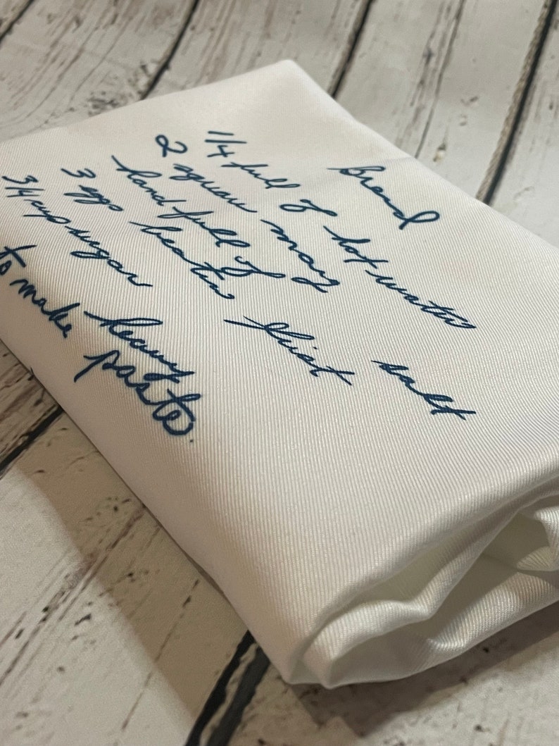 May include: A white fabric with blue ink handwritten instructions for making a recipe. The text reads "Brand Soy full of hot water 2 aguan beaten fist hand full of 3 egg sugar 5th aguan to make party."