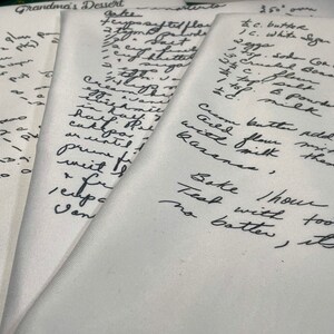 May include: Close-up of handwritten recipe cards with instructions for baking a cake. The recipe includes ingredients like butter, sugar, flour, and milk. The cards are on a white surface.