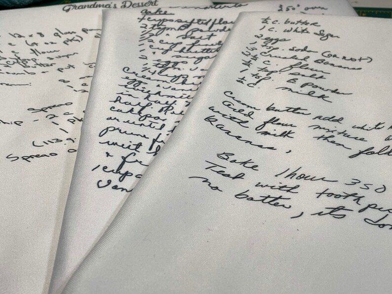 May include: Close-up of handwritten recipe cards with instructions for baking a cake. The recipe includes ingredients like butter, sugar, flour, and milk. The cards are on a white surface.