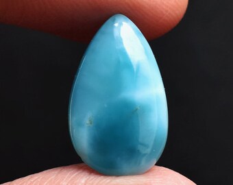 May include: A polished, pear-shaped cabochon gemstone featuring a vibrant sky-blue color with swirling white, cloud-like patterns throughout its smooth, glossy surface. The stone has a rounded top and a slightly wider base, reflecting light.