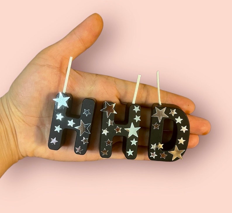 May include: Black letter candles with silver star accents spelling out "Happy".