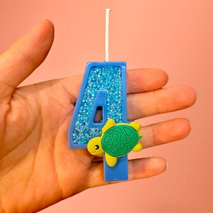 May include: Blue number four birthday candle with a glittery finish and a small green turtle decoration.