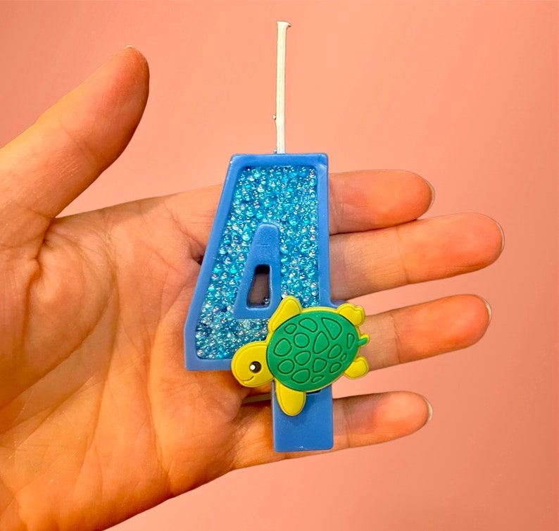 May include: Blue number four birthday candle with a glittery finish and a small green turtle decoration.