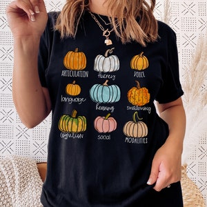 May include: Black t-shirt with a graphic of pumpkins and text that says "Articulation, Fluency, Voice, Language, Hearing, Swallowing, Cognition, Social, Modalities".