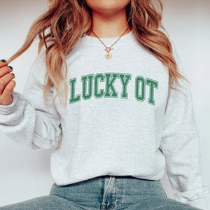 May include: A gray sweatshirt with the text "LUCKY OT" in green letters. The sweatshirt has a relaxed fit and is perfect for casual wear.