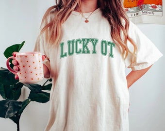 May include: A white t-shirt with the text "LUCKY OT" in green lettering. The shirt is oversized and has a relaxed fit.