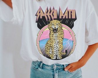 Puede incluir: Camiseta blanca con un gráfico de un leopardo en un círculo con rayos y el texto "Speech Path" en una fuente en negrita y estilizada.