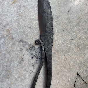 May include: A black forged knife with a curved handle and a serrated blade.