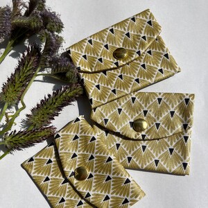 Könnte beinhalten: Drei kleine Stoffbeutel mit einem goldenen und schwarzen geometrischen Muster. Jeder Beutel hat einen goldenen Knopfverschluss.