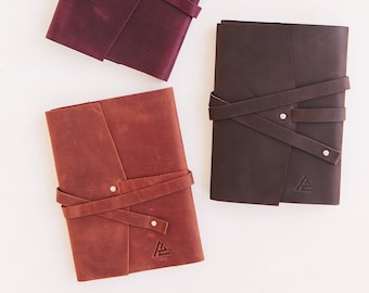 May include: Three leather-bound journals with a simple design. The journals are burgundy, brown, and orange. Each journal has a leather strap closure and a small metal triangle logo.