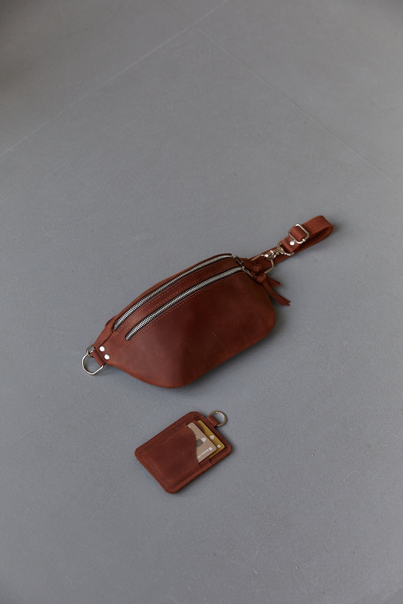 May include: A brown leather fanny pack with a zip closure and a detachable strap. A matching brown leather card holder with a silver ring is also included.