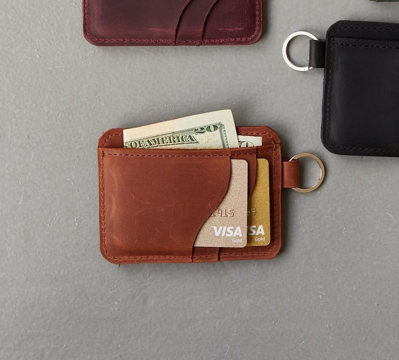 May include: A brown leather wallet with a card slot and a cash pocket. The wallet has a metal ring attached to it.