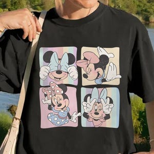 May include: Black t-shirt featuring a colorful graphic of Minnie Mouse in four different poses. Each pose is set within a pastel-colored square. The shirt is a casual style, suitable for everyday wear.