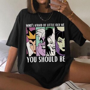 Puede incluir: Camiseta negra con un gr&aacute;fico de cuatro villanos de dibujos animados y el texto "WHO'S AFRAID OF LITTLE OLD ME YOU SHOULD BE". Los villanos est&aacute;n representados en un dise&ntilde;o colorido y estilizado.
