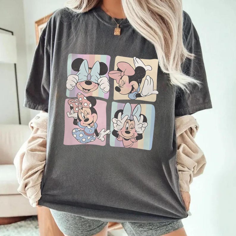 May include: Dark gray t-shirt featuring four squares with Minnie Mouse illustrations. Each square has a different pose and color scheme, including pastel backgrounds and bows. The shirt is a casual, oversized fit.