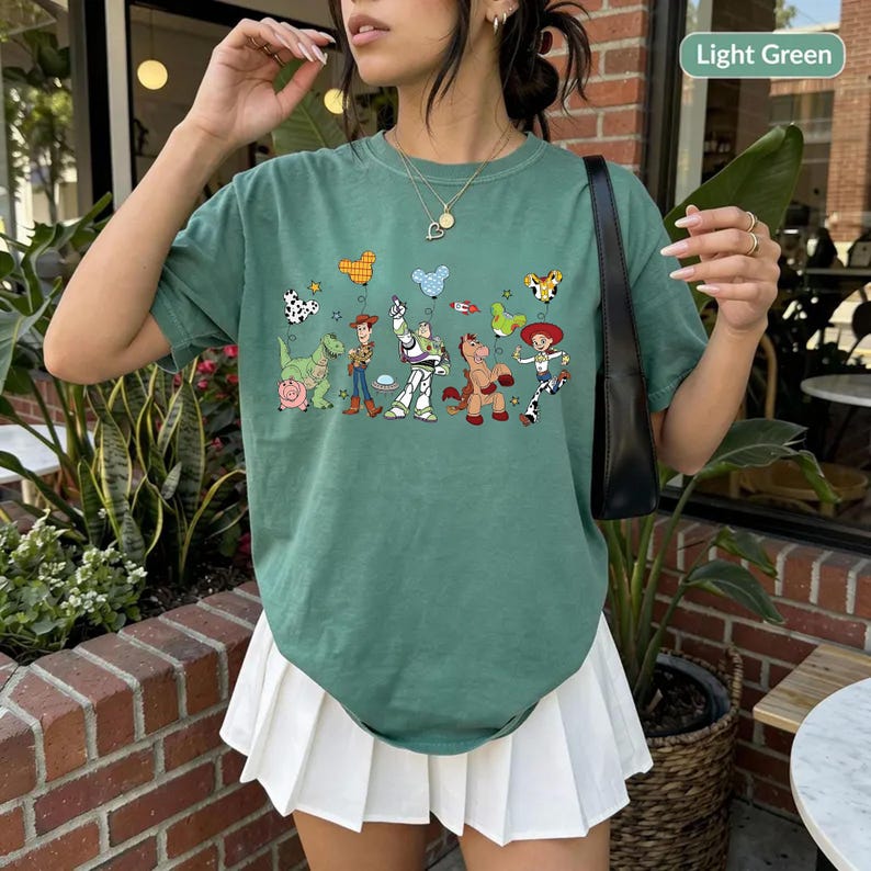 May include: Light green t-shirt featuring a colorful graphic of characters from a popular animated movie. The shirt has a crew neck and short sleeves. The text "Light Green" is in a white rectangle in the upper right corner.
