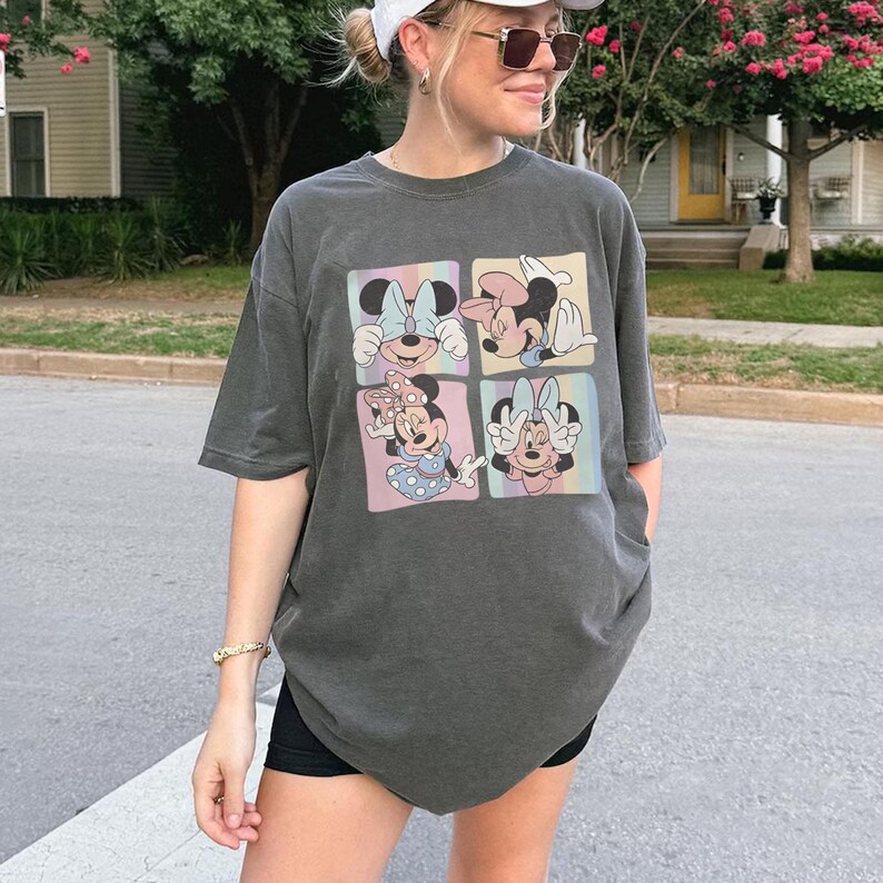 May include: Dark gray t-shirt featuring a four-panel graphic of Minnie Mouse in various poses. Each panel has a pastel rainbow background. The shirt is a relaxed fit and has short sleeves.