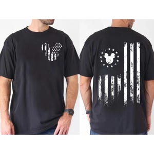 May include: Black t-shirt featuring a distressed American flag design with a Mickey Mouse silhouette. The front has the Mickey head outline with flag stripes. The back has a full flag design with the Mickey head and stars.