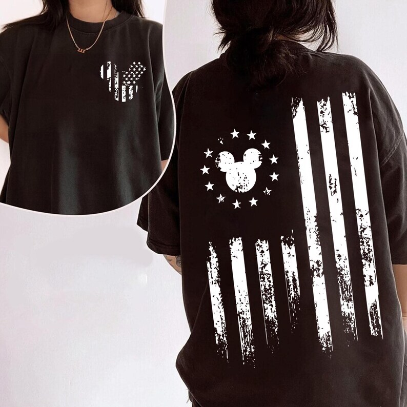 May include: Black t-shirt with a distressed white graphic of a Mickey Mouse-shaped American flag on the front and back. The back design features a Mickey Mouse head surrounded by stars and stripes.