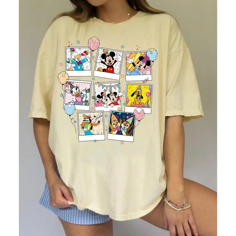 Puede incluir: Una camiseta amarillo claro con un collage de im&aacute;genes de personajes de dibujos animados en marcos estilo polaroid. Las im&aacute;genes incluyen Mickey Mouse, Minnie Mouse, Donald Duck y Pluto, con globos y estrellas de colores. La camiseta tiene mangas cortas y un corte holgado.