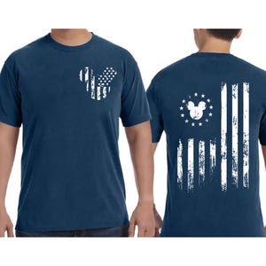 May include: Navy blue t-shirt featuring a distressed white graphic of the American flag in the shape of a mouse head on the front. The back of the shirt displays a similar design with the flag stripes and a mouse head surrounded by stars.