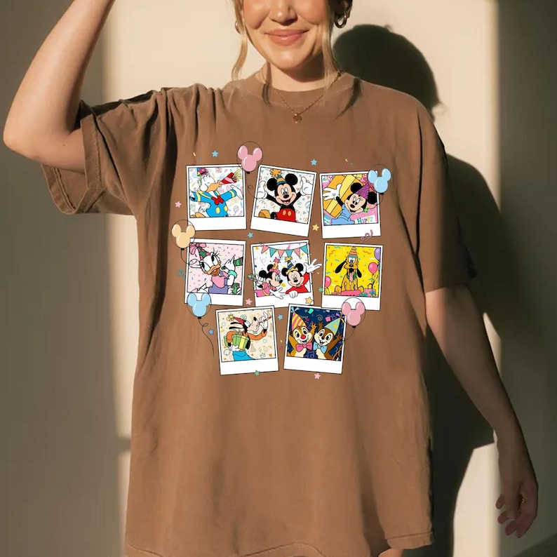 Puede incluir: Camiseta marr&oacute;n con un collage de im&aacute;genes de personajes de dibujos animados estilo polaroid. Las im&aacute;genes incluyen Mickey Mouse, Minnie Mouse, Donald Duck y otros personajes de Disney. Globos rosas y azules y estrellas decoran la camiseta.