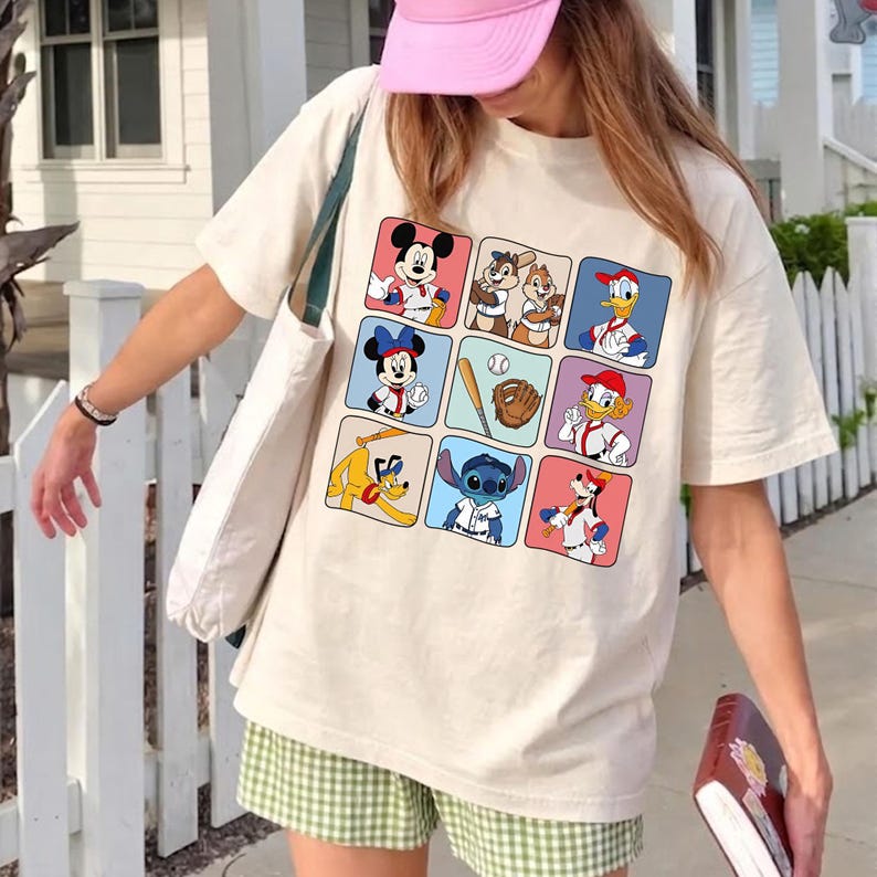 May include: Cream-colored t-shirt featuring a grid of cartoon characters in baseball uniforms. Mickey Mouse, Minnie Mouse, Chip and Dale, Donald Duck, Goofy, and Stitch are among the characters. A baseball, bat, and glove are also featured.