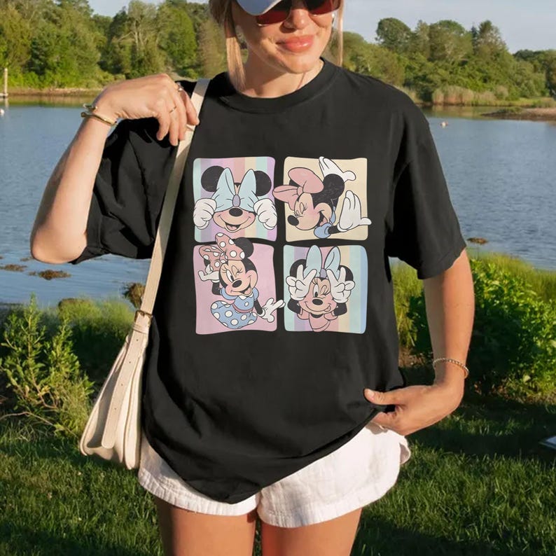 May include: Black t-shirt featuring a colorful graphic of Minnie Mouse in four different poses. Each pose is set within a pastel-colored square. The shirt is a casual style, suitable for everyday wear.