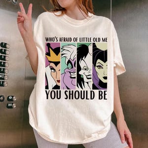 Puede incluir: Camiseta color crema con un gr&aacute;fico de cuatro villanos de dibujos animados y el texto "WHO'S AFRAID OF LITTLE OLD ME YOU SHOULD BE". El gr&aacute;fico incluye a la Reina Malvada, &Uacute;rsula, Cruella de Vil y Mal&eacute;fica.