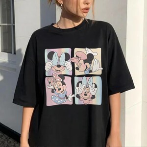 May include: Black t-shirt featuring a colorful graphic of Minnie Mouse in four different poses. Each pose is set within a square with a pastel rainbow background. The shirt has short sleeves and a relaxed fit.