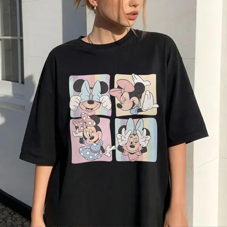 May include: Black t-shirt featuring a colorful graphic of Minnie Mouse in four different poses. Each pose is set within a square with a pastel rainbow background. The shirt has short sleeves and a relaxed fit.