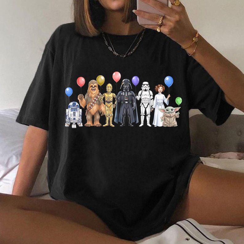 May include: Black t-shirt with a graphic of Star Wars characters holding balloons. The characters include R2-D2, Chewbacca, C-3PO, Darth Vader, a Stormtrooper, Princess Leia, and Grogu.