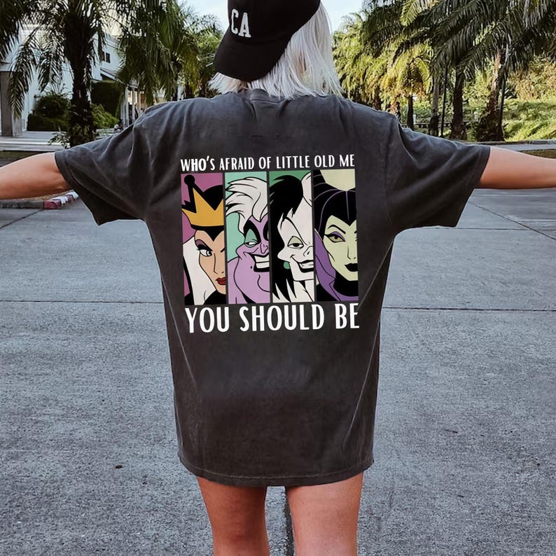 Puede incluir: Camiseta gris oscuro con un gr&aacute;fico de cuatro villanos de dibujos animados y el texto "WHO'S AFRAID OF LITTLE OLD ME YOU SHOULD BE". El gr&aacute;fico incluye im&aacute;genes de una reina, &Uacute;rsula, Mal&eacute;fica y otro villano.