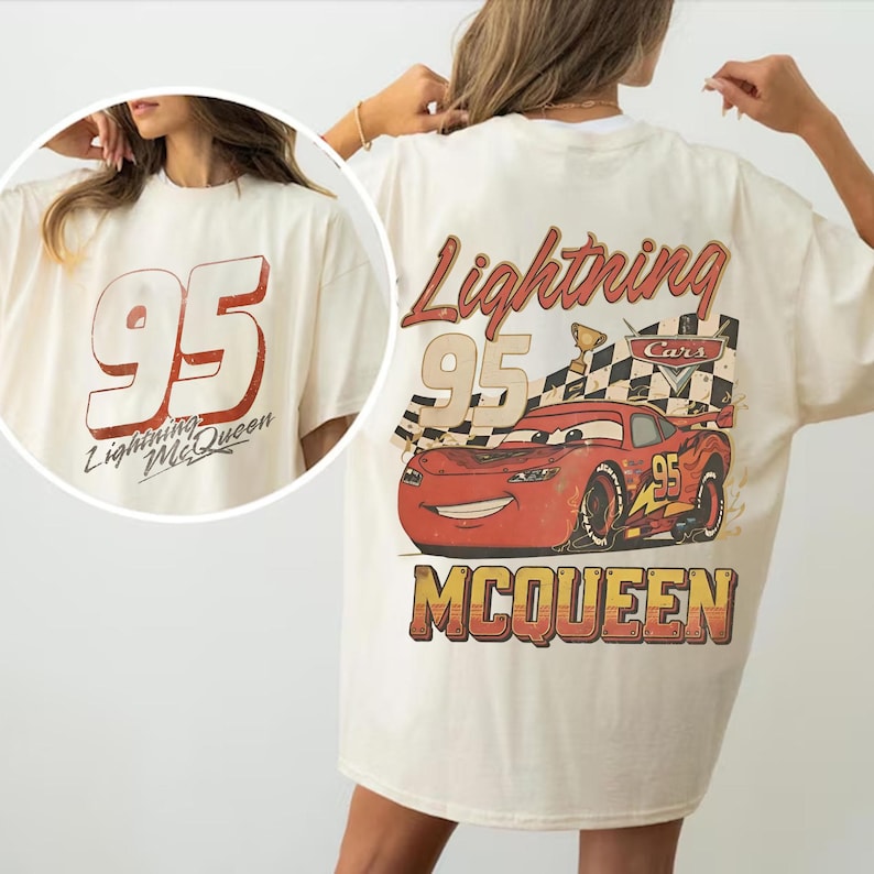 May include: Cream-colored t-shirt featuring a graphic of Lightning McQueen from the Cars movie. The design includes the number 95, the words "Lightning McQueen," and a checkered flag. The shirt has a vintage, distressed look.
