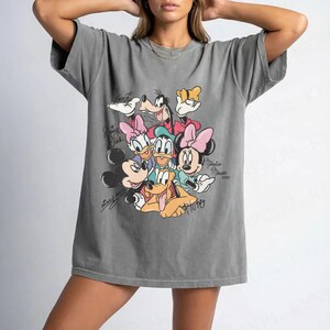 May include: Gray t-shirt featuring a graphic of Disney characters including Mickey Mouse, Minnie Mouse, Donald Duck, Daisy Duck, Goofy, and Pluto. The graphic has a vintage style with the characters' names in cursive.