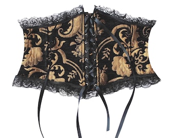May include: A black and gold corset with a floral pattern. The corset has a lace-up front and black lace trim along the top and bottom edges. Black ribbons hang from the bottom. The corset is designed to cinch the waist.