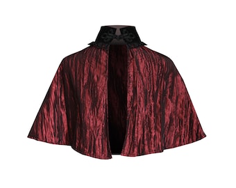 May include: A red velvet cape with a black velvet collar and lace trim. The cape has a gathered look and is open in the front.