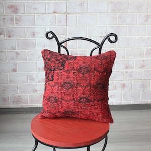 May include: Red and black patterned throw pillow on a red chair with a black metal frame. The chair is in front of a white brick wall.